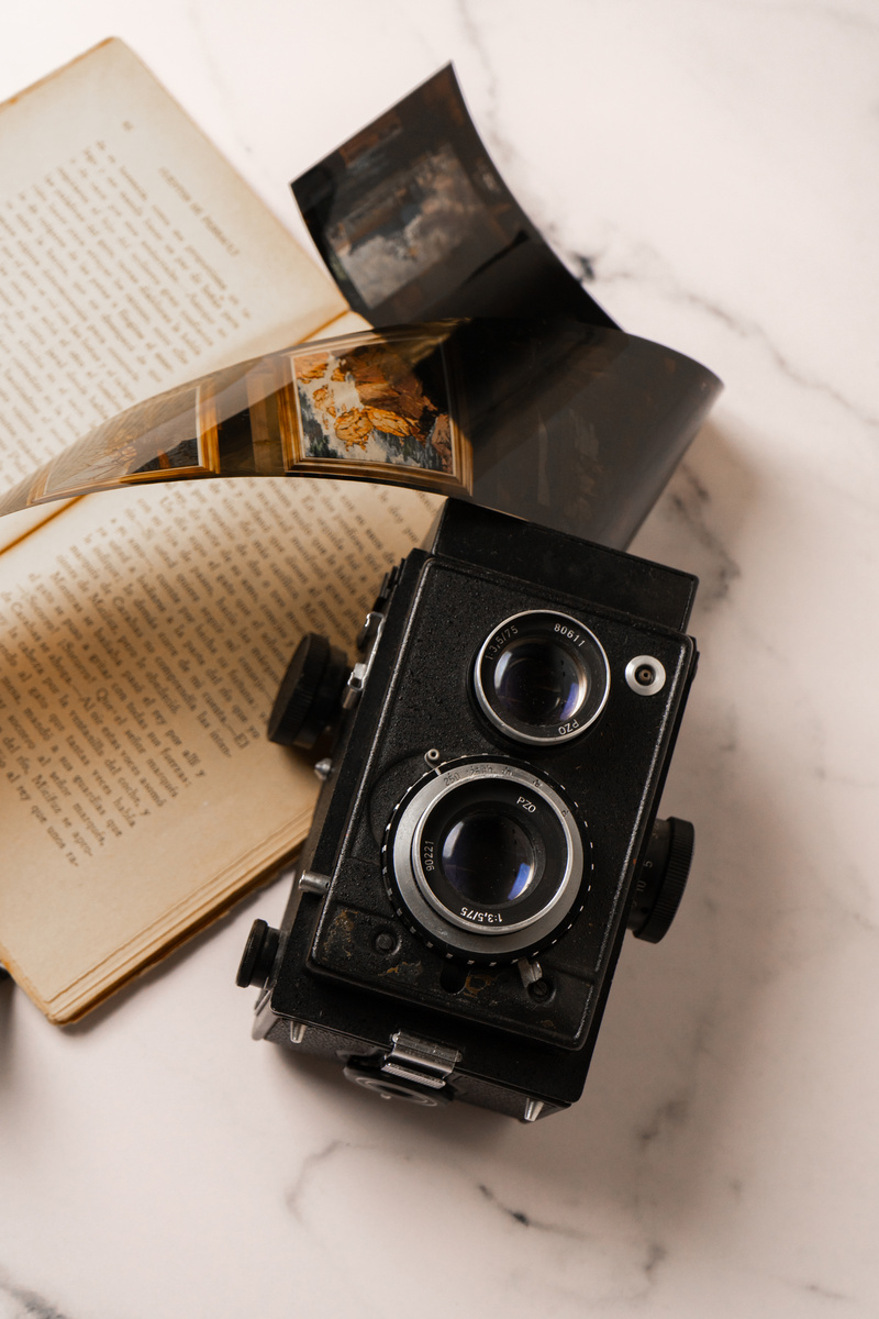 Camera, Film Negative and Book on Marble Background
